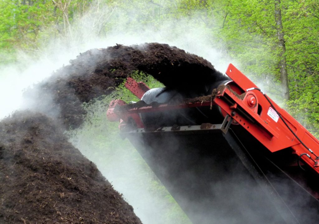 Large red mechanical compost mixer with steam coming from the compost